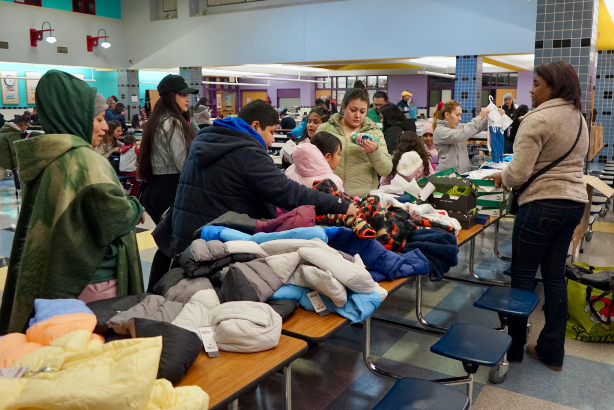 Families viewing items like coats and jackets that are laid out on a cafeteria table at the Sokolowski School